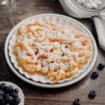 The funnel cake with pancake mxi is on a plate with blueberries surrounding it.