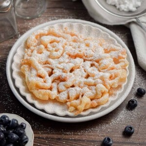 The funnel cake with pancake mxi is on a plate with blueberries surrounding it.