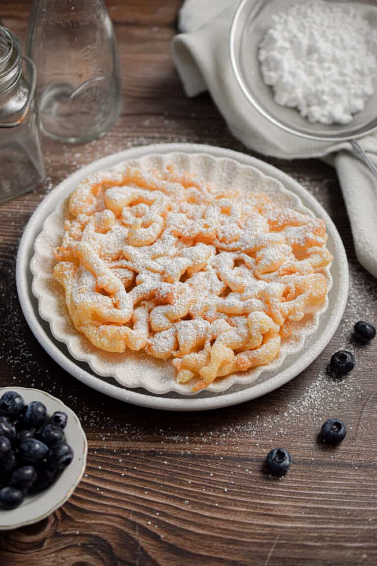 The funnel cake with pancake mxi is on a plate with blueberries surrounding it.
