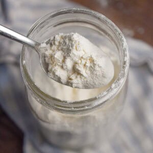A spoon is lifting the self rising flour out of the mason jar.