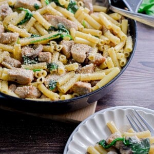 The large skillet full of pork tenderloin pasta is shown with a fluted plate with a small portion of the pasta on the plate.