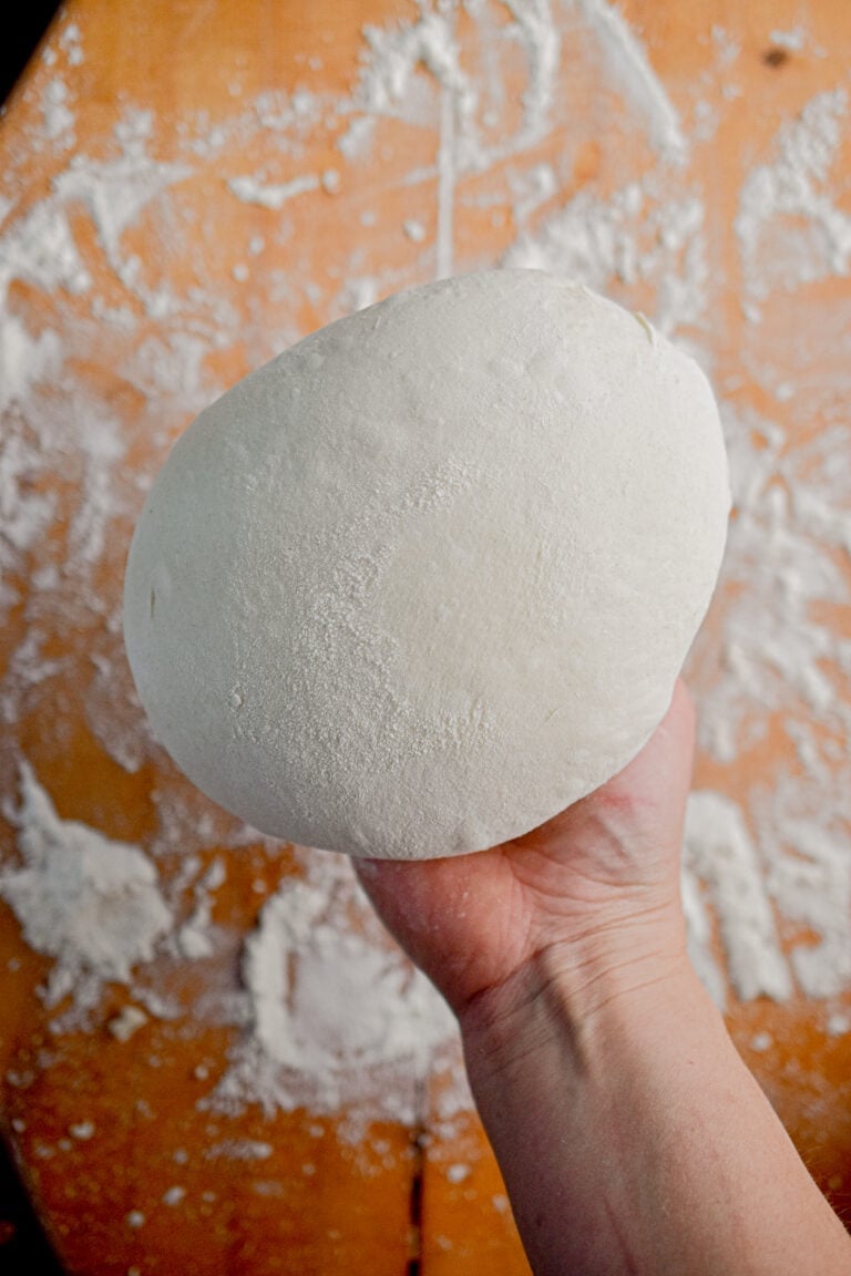 A hand is holding a fully shapes sourdough boule.
