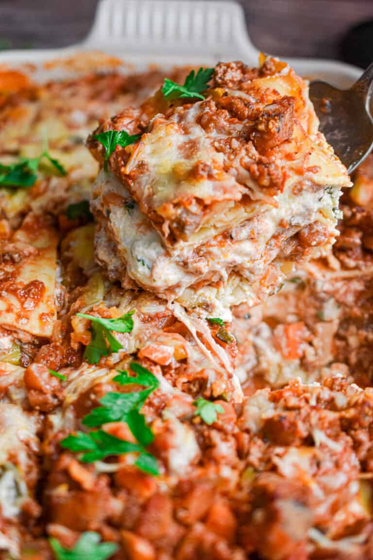 A piece of the meat and vegetable lasagna is being taken out of the lasagna pan.