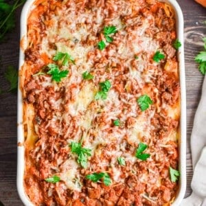 The meat and vegetable lasagna is topped with fresh parsley and surrounded by a tan napkin.
