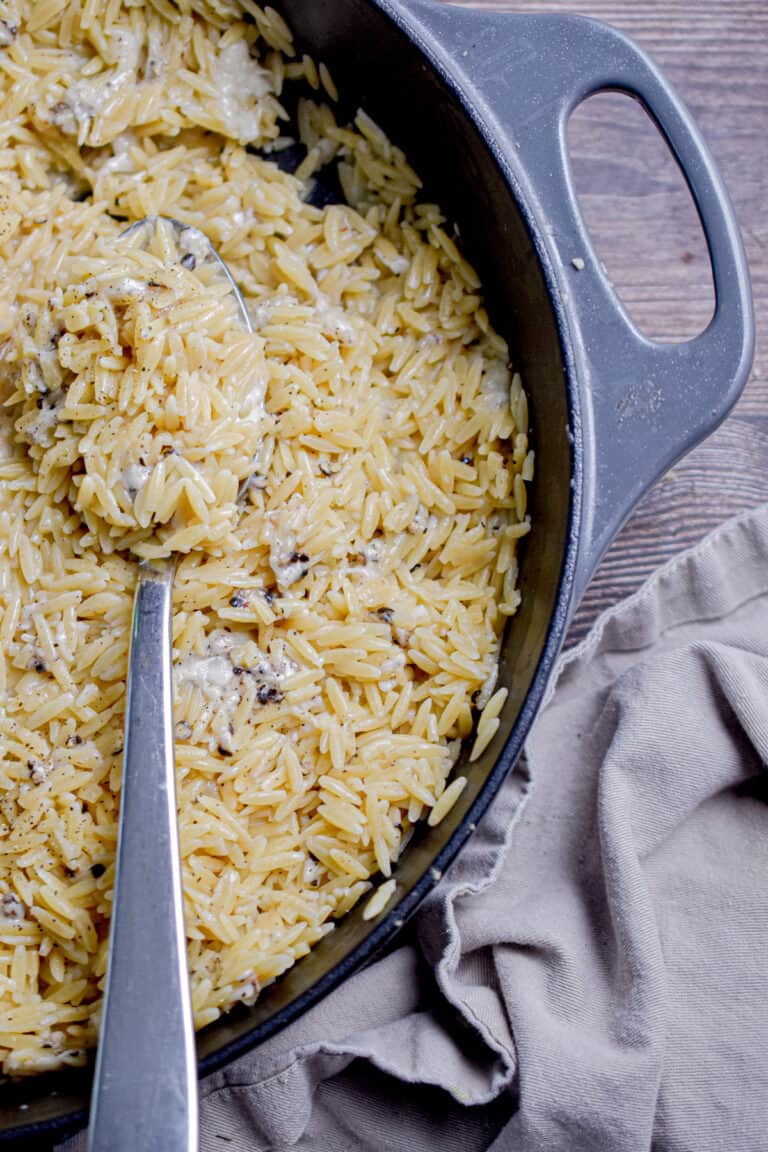 A spoon is laying in the pan of orzo cacio e pepe.