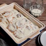 The sourdough discard cinnamon rolls are in a blue baking dish with glass bottles in the background.