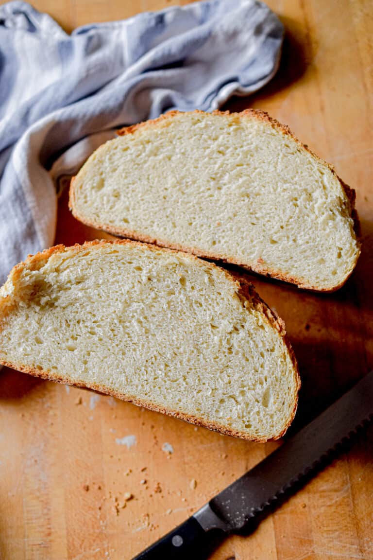 A loaf of sourdough bread is cut in half with a blue napkin and a serrated knife shown.