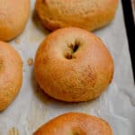 A whole wheat sourdough bagel is on a parchment lined baking sheet.
