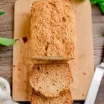 The banana bread with cake flour is on a board with a serrated knife.