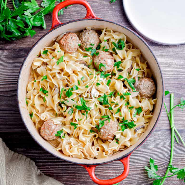 The one pot meatball stroganoff is in a red Dutch oven with parsley around it.