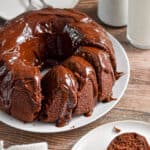 The sourdough chocolate cake is on a white plate with a piece of the cake on a plate being cut by a fork.