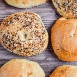 An everything sourdough discard bagel is next to five other bagels on a wooden background.