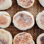 Nine sourdough English muffins are laid out on a wire rack over a baking sheet.