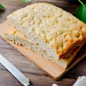 The sourdough discard focaccia is on a wooden cutting board with a serrated knife in front of it.