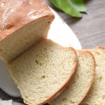 The sourdough discard sandwich bread is on a white cutting board with a plant in the background.