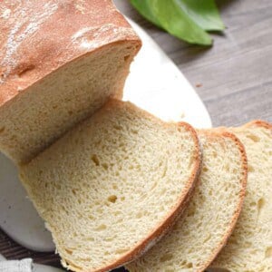 The sourdough discard sandwich bread is on a white cutting board with a plant in the background.