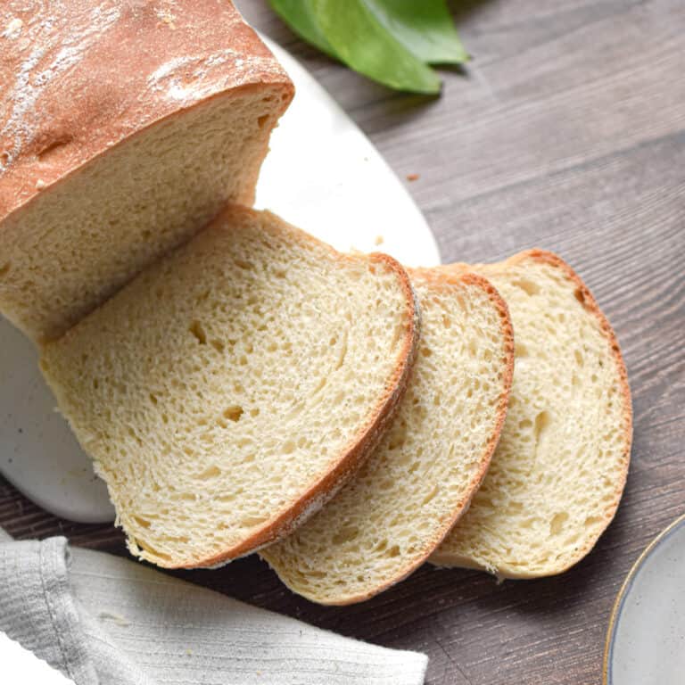 The sourdough discard sandwich bread is on a white cutting board with a plant in the background.