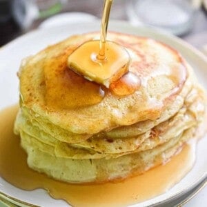 Maple syrup is being poured over a stack of sourdough banana pancakes.