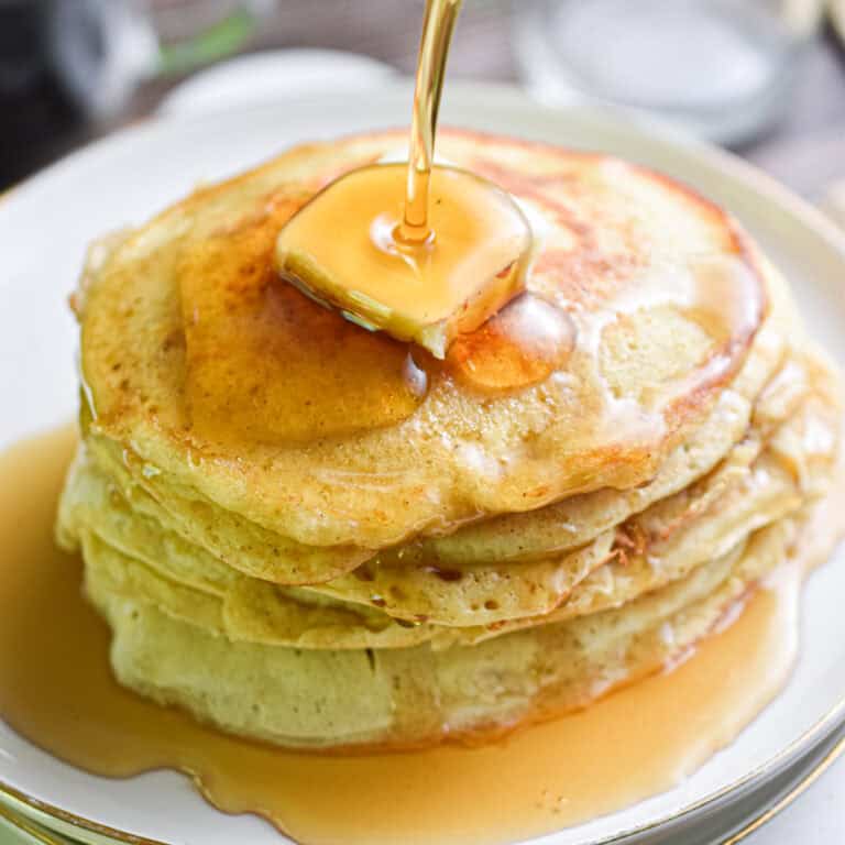 The sourdough banana pancakes are stacked and then the maple syrup is being poured over it.