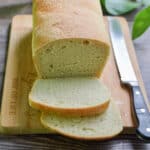 The sourdough sandwich bread is sliced and on a wooden cutting board with a serrated knife next to the bread.