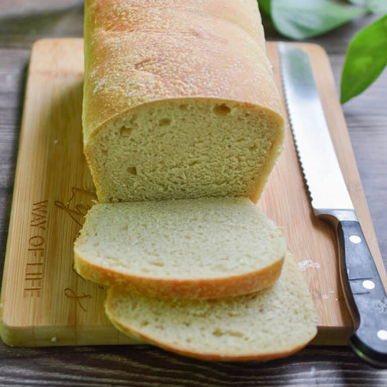The sourdough sandwich bread is sliced and on a wooden cutting board with a serrated knife next to the bread.