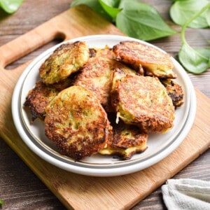The sourdough zucchini fritters are on a cutting board in a white plate with a green plant in the back.