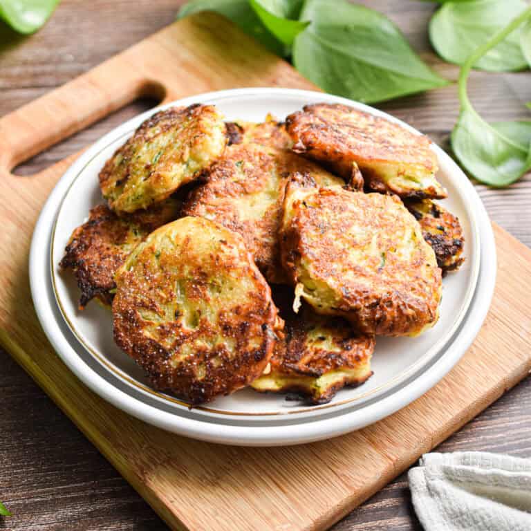 A plate of sourdough zucchini fritters is on a cutting board with a green plant in the background.