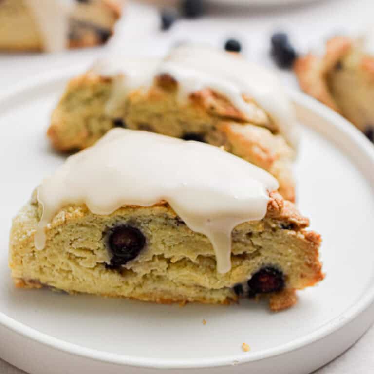 Two sourdough blueberry scones are on a plate with a glaze on top of them.