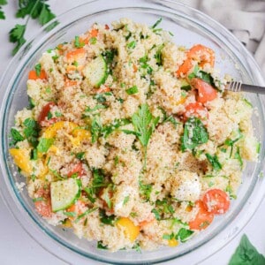 The Summer couscous salad is in a glass bowl surrounded by more basil and a napkin.