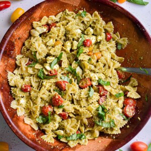 The pesto pasta salad is in a wooden bowl surrounded by tomatoes.