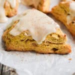 A pumpkin sourdough scone is topped with a glaze and a sprinkle of cinnamon.