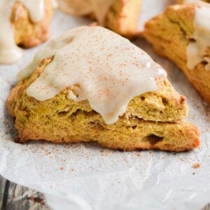 A pumpkin sourdough scone is topped with a glaze and a sprinkle of cinnamon.