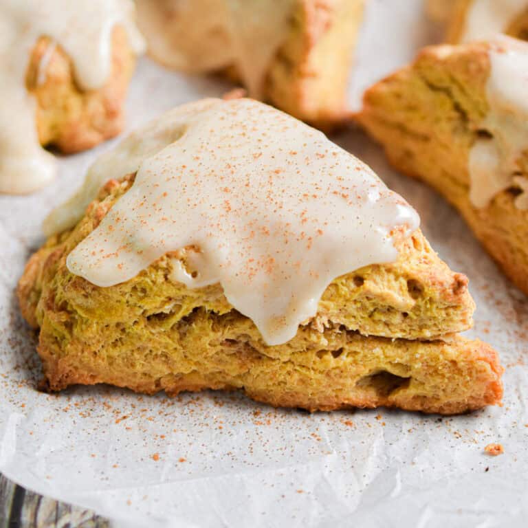 A pumpkin sourdough scone is topped with a glaze and a sprinkle of ground cinnamon.