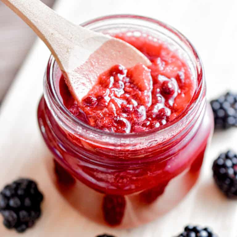 A wooden spoon is lifting the blackberry syrup for pancakes out of the mason jar.