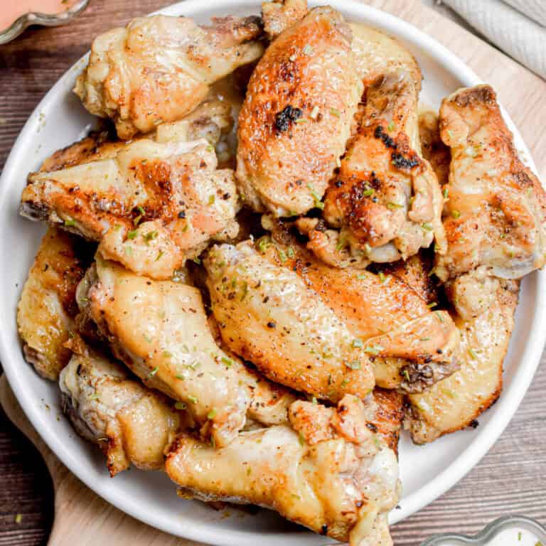 A platter of wings is on a circle plate sprinkles with chives.