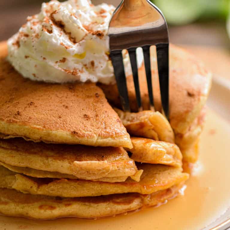 A fork is taking a piece of the stack of sourdough pumpkin pancakes.