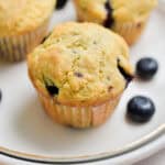 A blueberry muffins with self rising flour is on a plate surrounded by other muffins and blueberries.