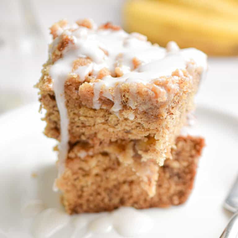 Two pieces of banana coffee cake are stacked on top of each other with bananas in the background.