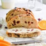 The cranberry orange sourdough bread is sliced and surrounded by cranberries and slices of oranges.
