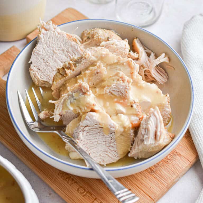 The Instant Pot turkey breast is in a bowl on a cutting board surrounded by a cloth napkin.