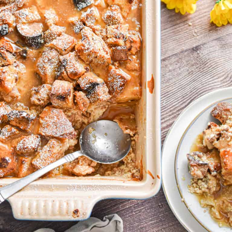 A spoon is in the pan with the sourdough bread pudding and a portion of the pudding is on a plate.