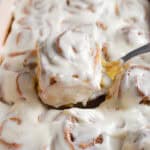 A spatula is holding one sourdough pumpkin cinnamon roll out of the pan.