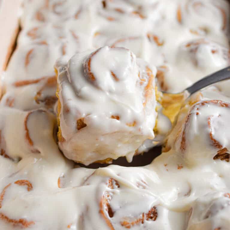 A spatula is holding one sourdough pumpkin cinnamon roll out of the pan.