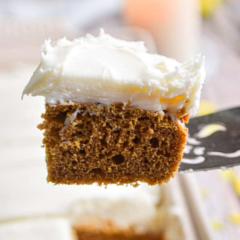 A pie holder is holding a piece of the sourdough pumpkin cake topped with cream cheese icing.
