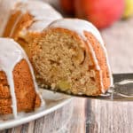 The sourdough apple cake is topped with powdered sugar icing and a slice is being taken out of the cake.