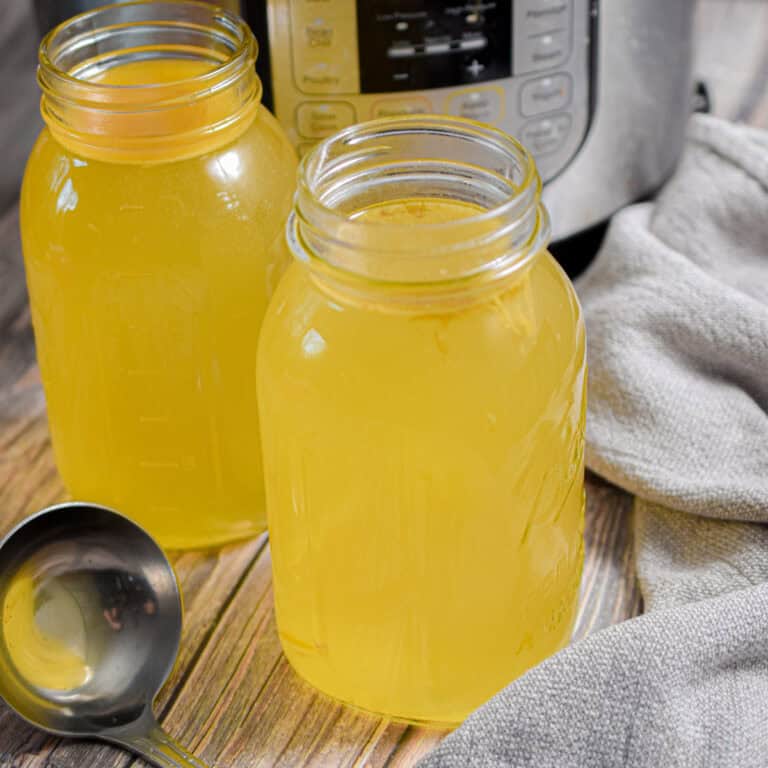 Two mason jars full of Instant Pot Turkey Broth are in front of an Instant Pot.