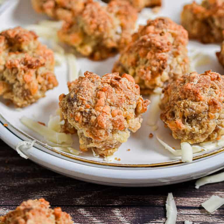 The Bisquick sausage balls are on a white plate surrounded by shredded cheese.