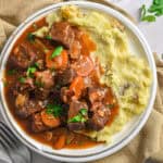 The Instant Pot beef bourguignons is on a plate of mashed potatoes.