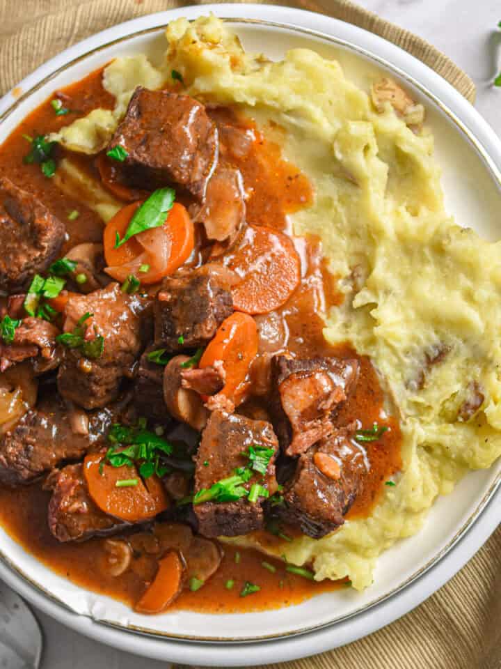 The Instant Pot beef bourguignons is on a plate of mashed potatoes.