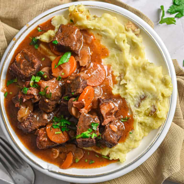 The Instant Pot beef bourguignons is on a plate of mashed potatoes.